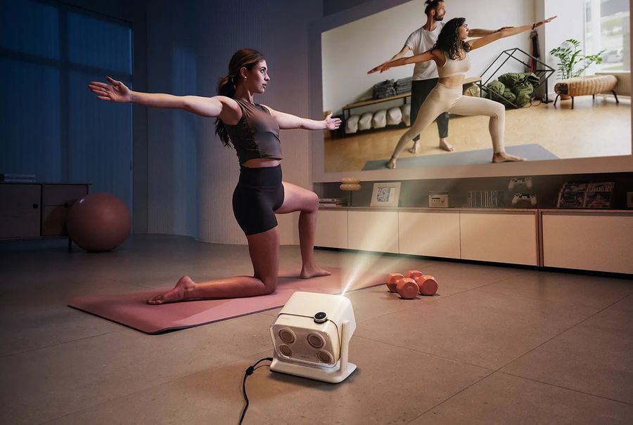 Projecteur Aurzen BOOM mini diffusant un cours de sport sur grand &eacute;cran dans un salon pour une s&eacute;ance d&rsquo;entra&icirc;nement &agrave; domicile.