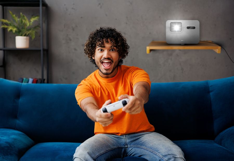 Un homme joue à un jeu vidéo avec un vidéoprojecteur 4K LED BenQ TK705i en arrière-plan affichant une image fluide.