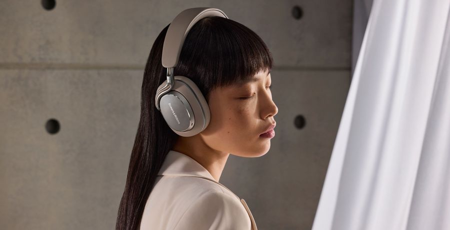 Casque Bluetooth Bowers & Wilkins PX8 S2 porté par une personne debout contre un mur en béton éclairé latéralement.