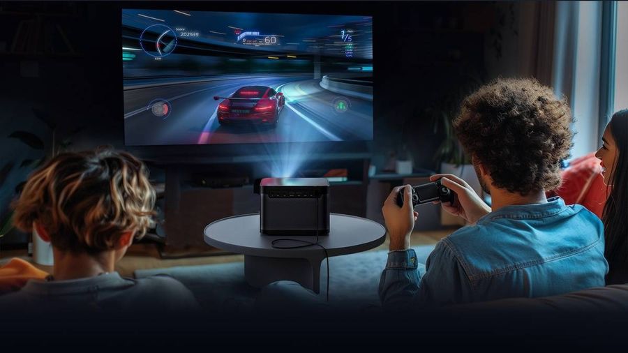 Le vidéoprojecteur laser 4K Dangbei Mars Pro 2 projette un jeu de course sur un écran, tandis que trois personnes jouent.
