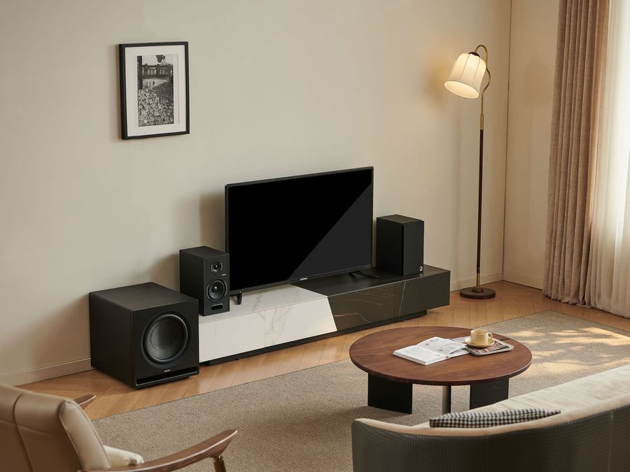 Caisson de basses Elipson Premium SUB 12 Caisson de basses Elipson Premium SUB 12 noir, positionné dans un salon moderne à côté d'une enceinte et d'un téléviseur.