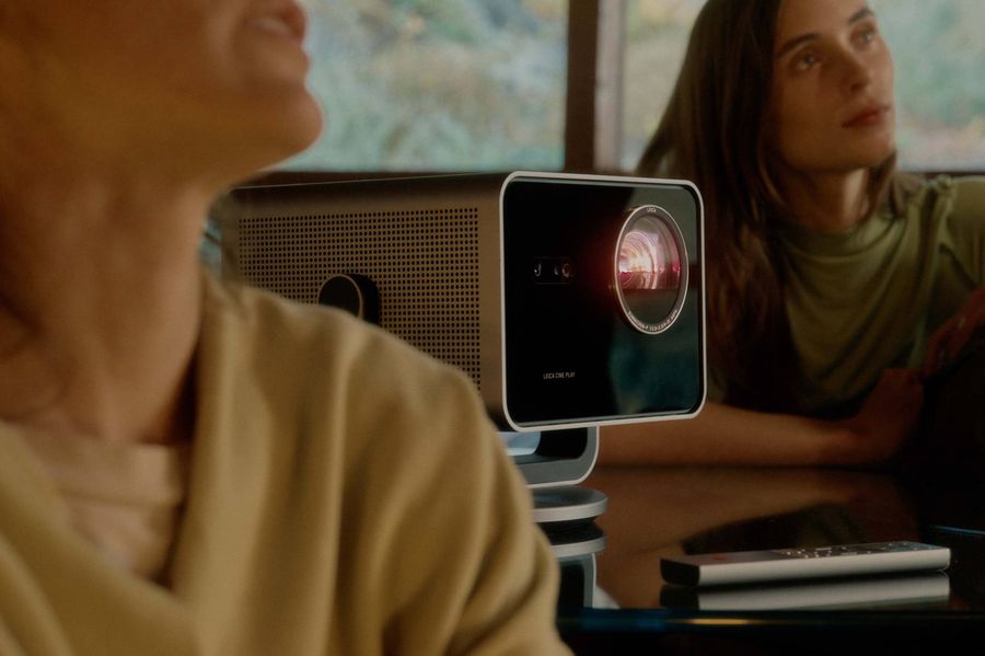 Projecteur Leica Cine Play 1 sur une table avec deux personnes en arrière-plan regardant vers l'écran.