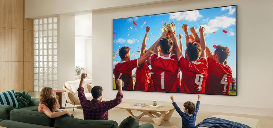 T&eacute;l&eacute;viseur Mini LED LG 100QNED87B install&eacute; dans un salon familial, diffusant un match de football c&eacute;l&eacute;br&eacute; par les joueurs.