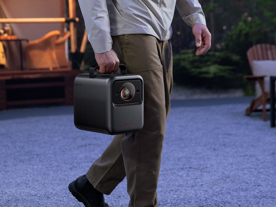  Un homme transporte un vidéoprojecteur triple laser 4K Nebula X1, conçu pour un usage nomade en extérieur.