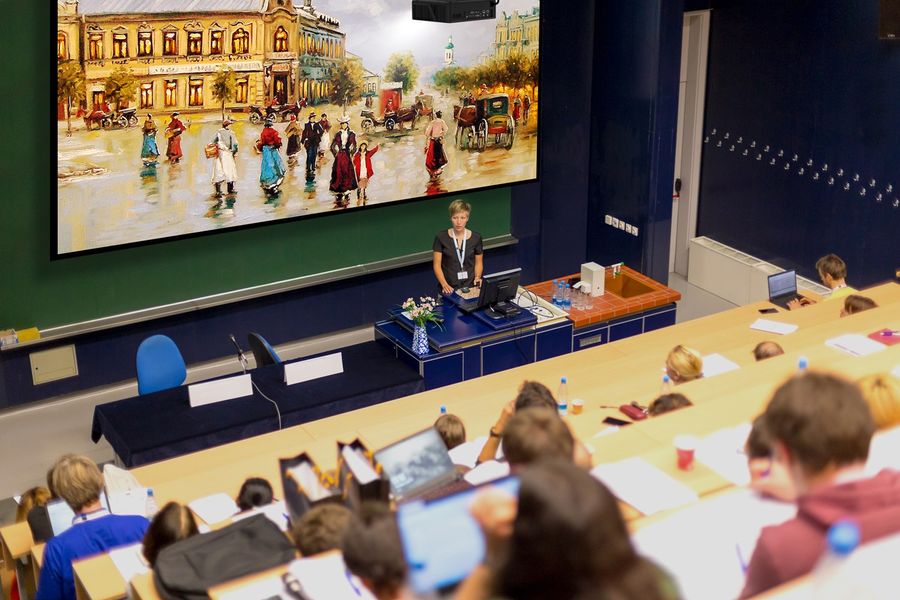 Projecteur Optoma ZU507TST en amphithéâtre  Amphithéâtre universitaire équipé d’un projecteur Optoma ZU507TST diffusant une peinture numérique sur grand écran au-dessus de l’enseignante.