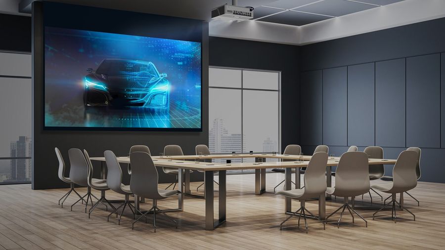 Projecteur Optoma ZU707T en salle de réunion  Salle de réunion moderne équipée d’un projecteur Optoma ZU707T affichant une image numérique de voiture futuriste en haute définition.