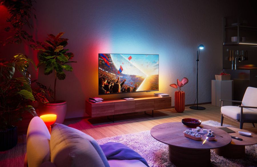 T&eacute;l&eacute;viseur LED 4K Philips 65PUS8001 install&eacute; dans un salon moderne, diffusant un &eacute;v&eacute;nement sportif avec un &eacute;clairage d'ambiance color&eacute; synchronis&eacute;.