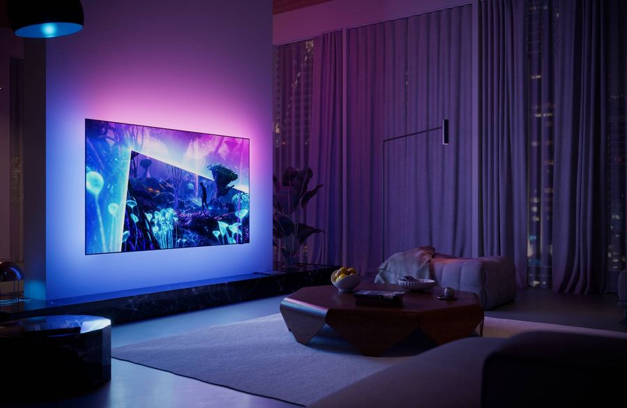 T&eacute;l&eacute;viseur OLED Philips 77OLED951 install&eacute; dans un salon sombre, avec &eacute;clairage Ambilight color&eacute; diffus&eacute; autour de l&rsquo;&eacute;cran.