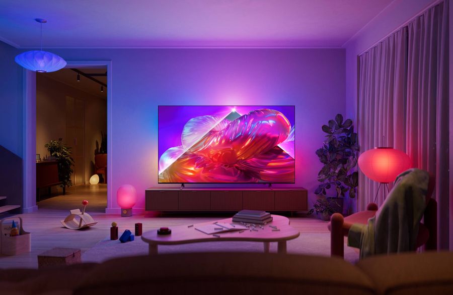 T&eacute;l&eacute;viseur Philips 85PQS9001 The One avec Ambilight affichant une image color&eacute;e dans un salon moderne &agrave; l'&eacute;clairage d'ambiance.