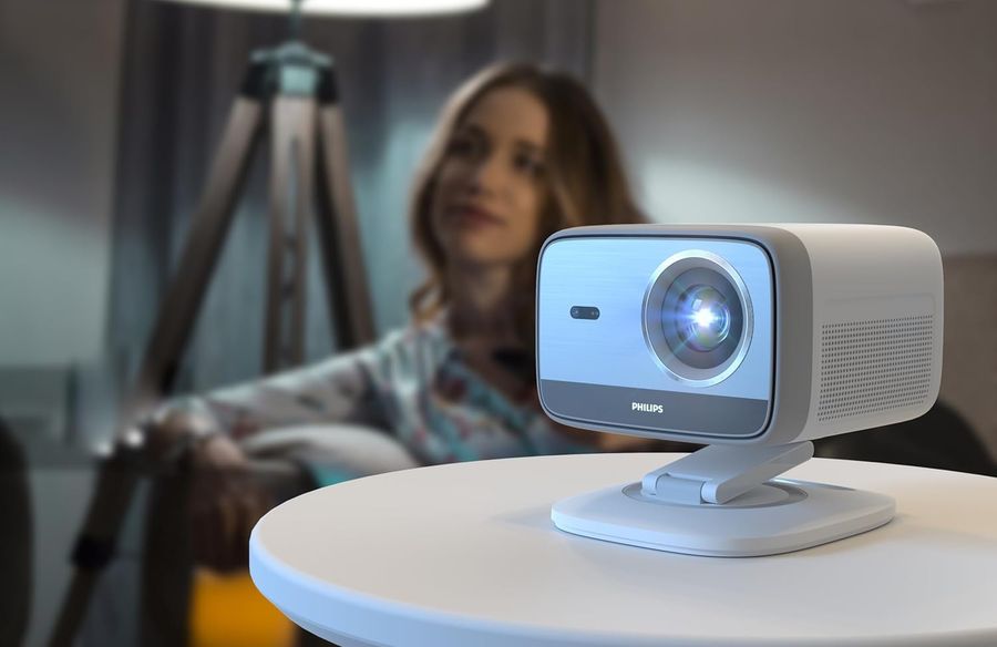 Vid&eacute;oprojecteur Full HD compact Philips NeoPix 444 pos&eacute; sur une table, projetant une image lumineuse dans un salon.