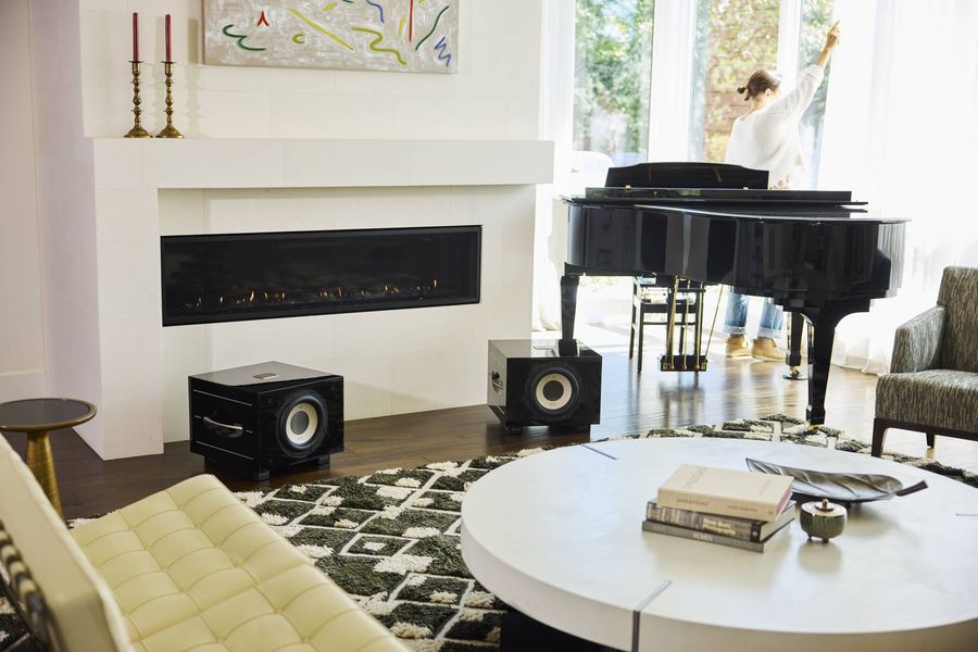 Deux caissons de basses REL Acoustics S/550 sont installés dans un salon contemporain avec piano et cheminée.