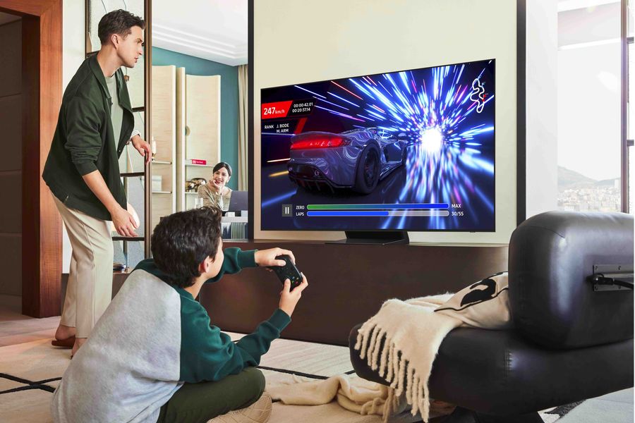  Téléviseur OLED Samsung TQ65S90F affichant un jeu vidéo de course, utilisé dans un salon familial moderne.