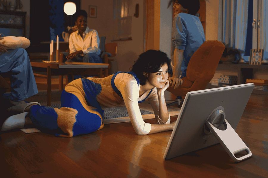 Femme allong&eacute;e regardant un &eacute;cran connect&eacute; Samsung The MovingStyle 27LSM7FA pos&eacute; au sol dans un salon convivial.