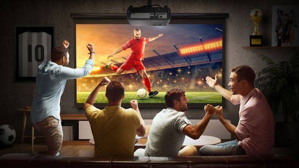 Vid&eacute;oprojecteur triple laser 4K ViewSonic LX720-4KB RGB projetant un match de football sur grand &eacute;cran dans un salon convivial.