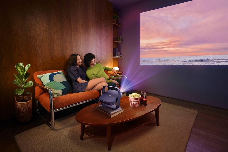 Projecteur Xgimi Elfin Flip Laser HD projetant une grande image dans un salon, tandis que deux personnes regardent un contenu confortablement install&eacute;es.