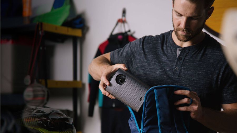 Un homme range un vidéoprojecteur Xgimi Halo+ Google TV portable dans un sac à dos bleu.