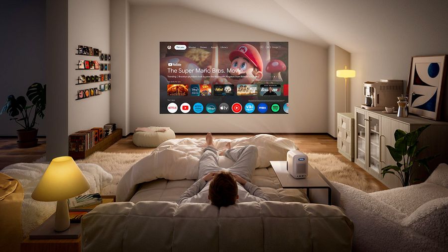 Projecteur Full HD compact Xming Episode Two projette interface multim&eacute;dia sur grand mur dans salon cosy avec &eacute;clairage tamis&eacute;.